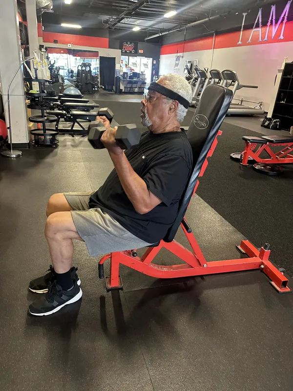 Member doing seated dumbbell curls on red bench