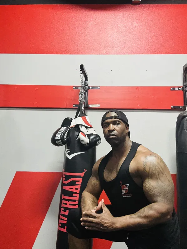 Coach Mugz — Founder of Fitness Explosion Elite Training, standing by heavy bag